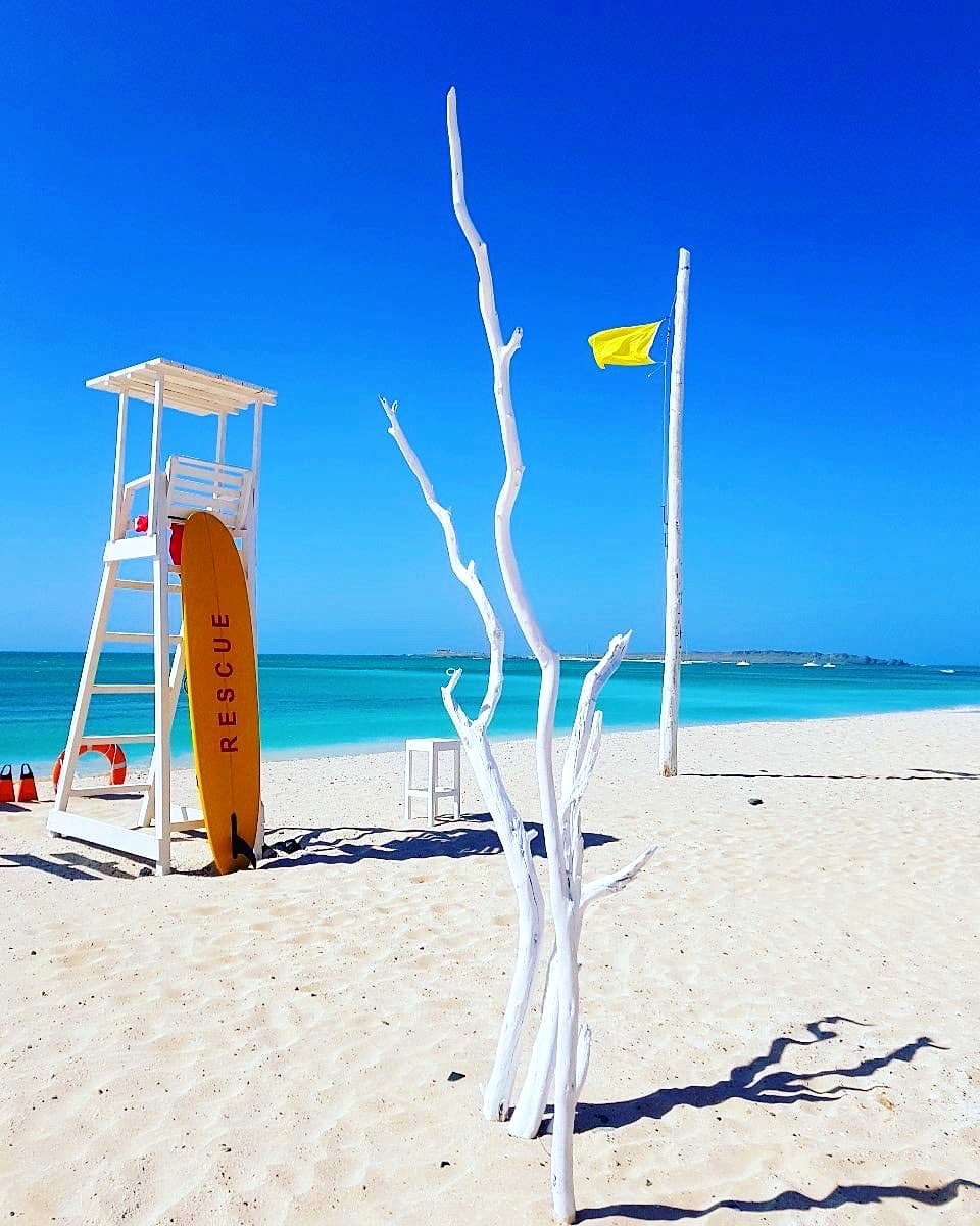 Torretta di salvataggio bianca e tavola gialla «Rescue» su una spiaggia di sabbia bianca, davanti al mare turchese di Boa Vista