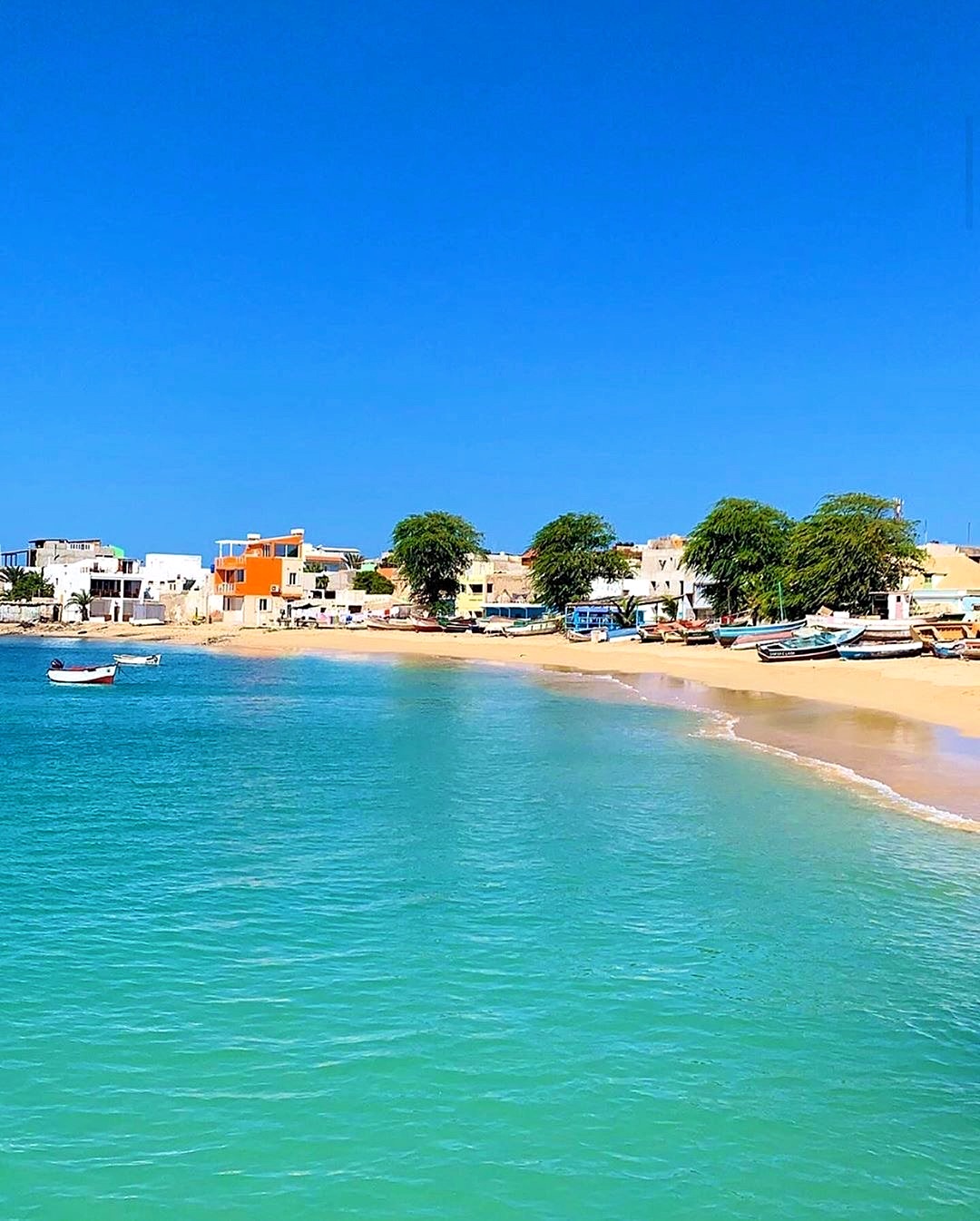 Baia con le barche dei pescatori e le case colorate affacciate su un mare turchese chiarissimo, a Boa Vista