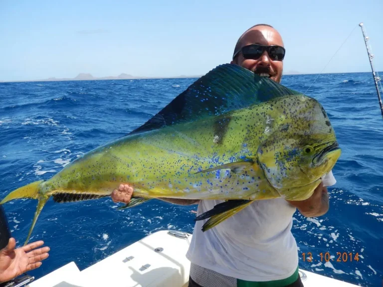 Pescatore con una grande lampuga e l'oceano alle spalle