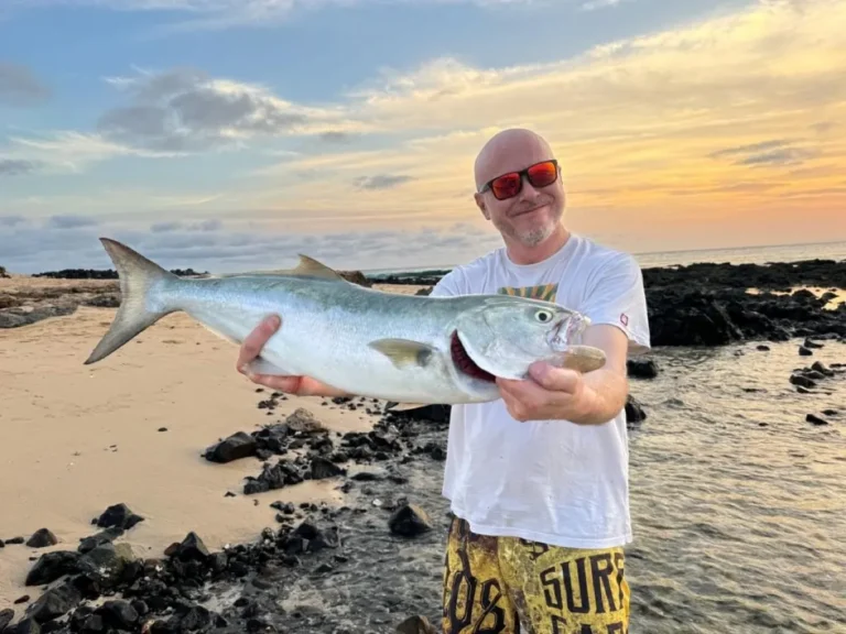 Pescatore sugli scogli al tramonto con un pesce serra