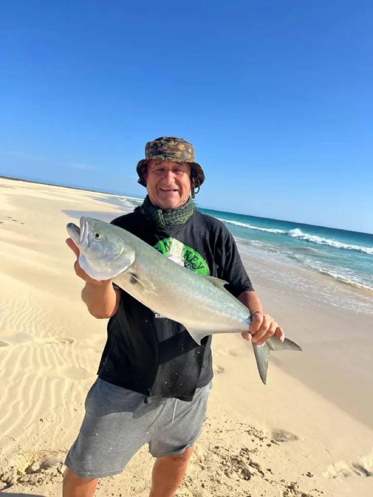 Pescatore sulla spiaggia deserta con un pesce serra